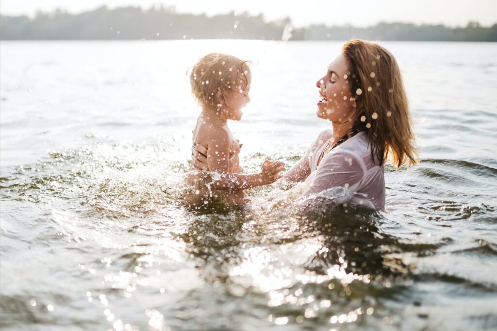 side view of happy mother and daughter swimming in river